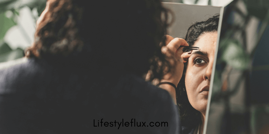 A woman plucking her eyebrows in mirror.