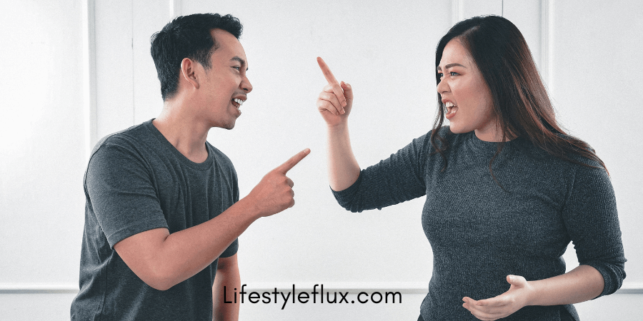 A man and a woman are facing each other, both with open mouths and pointing fingers, suggesting a heated argument.